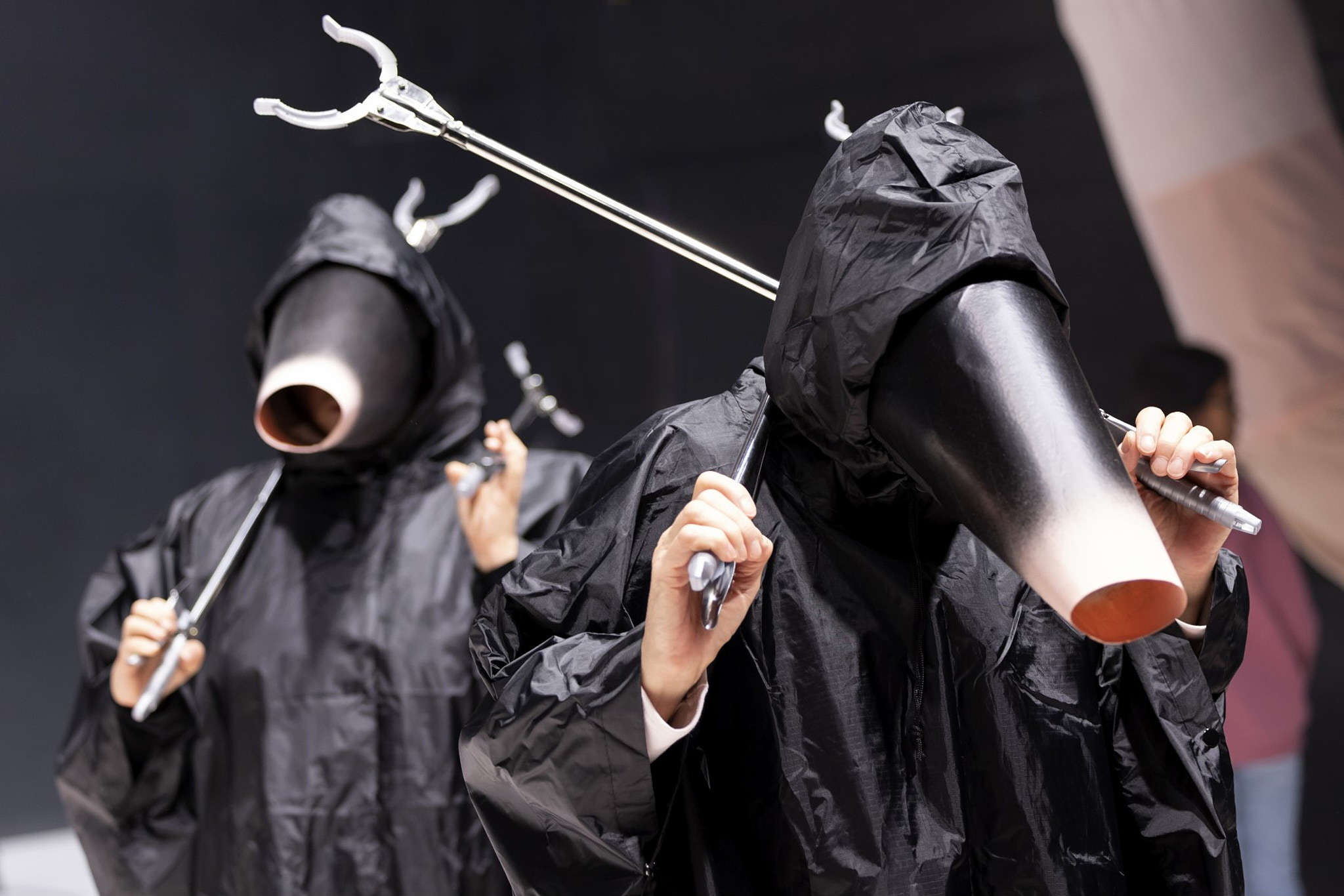 Zwei maulwurfsartige Wesen in schwarzen Umhängen halten jeweils zwei Greifarme.