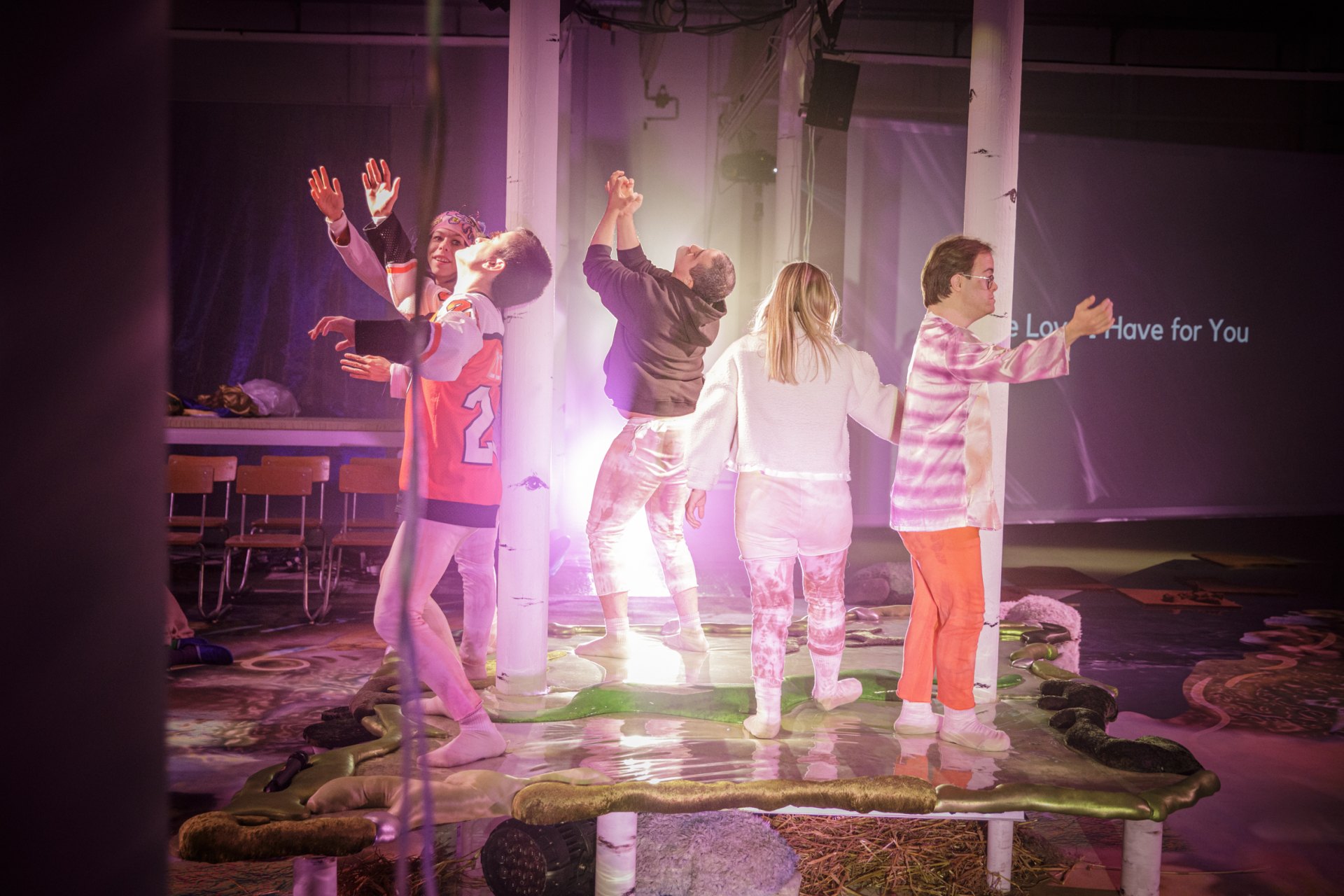 Auf einem grünen Plüschuntergrund tanzen fünf Personen. Sie stehen im Kreis, dem Publikum zugewandt. Die helle Beleuchtung zeichnet die Szene weich. Auf einer Leinwand im Hintergrund steht: "The Love I Have for You".